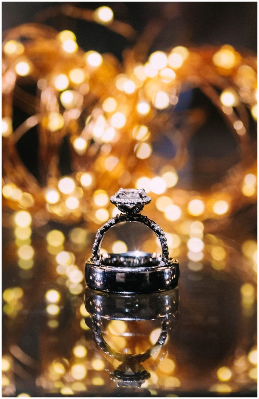 Premier snohomish & seattle wedding photographer | gsquared weddings photography a diamond engagement ring and wedding band are stacked together on a reflective surface with warm out of focus string lights glowing in the backgroundcapturing the magic of a snohomish seattle wedding engagement | serving snohomish seattle                   & beyond