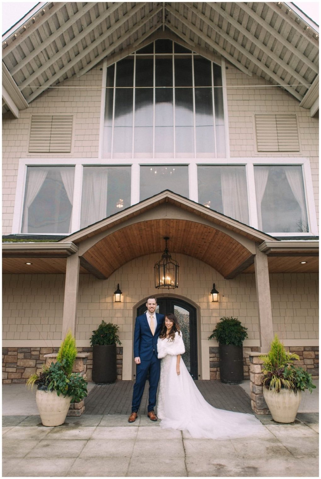 Premier snohomish & seattle wedding photographer | gsquared weddings photography a bride and groom stand together under the entrance of a large building with a peaked roof large windows and potted plants on either sidea beautiful moment from their snohomish seattle wedding The bride wears a white gown the groom wears a blue suit | serving snohomish seattle                   & beyond