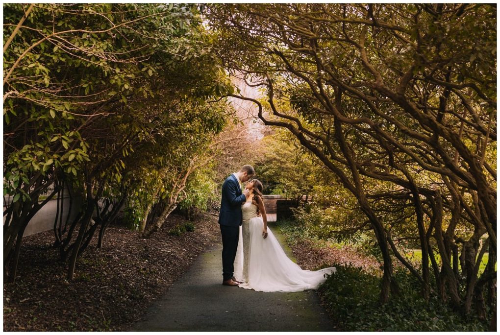 Premier snohomish & seattle wedding photographer | gsquared weddings photography a bride and groom stand close together on a path beneath arching trees in snohomish surrounded by lush greenery The groom kisses the brides forehead as she gently touches his chest creating an intimate romantic moment | serving snohomish seattle                   & beyond