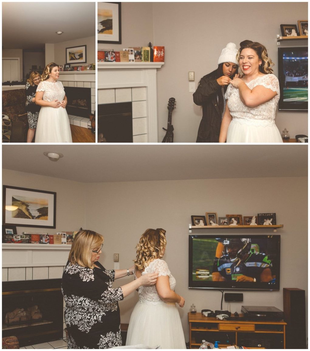 Premier snohomish & seattle wedding photographer | gsquared weddings photography a bride in a white dress gets ready with help from two women in a cozy snohomish living room with a tv showing a football game a fireplace and family photos on the mantle before her seattle wedding | serving snohomish seattle                   & beyond