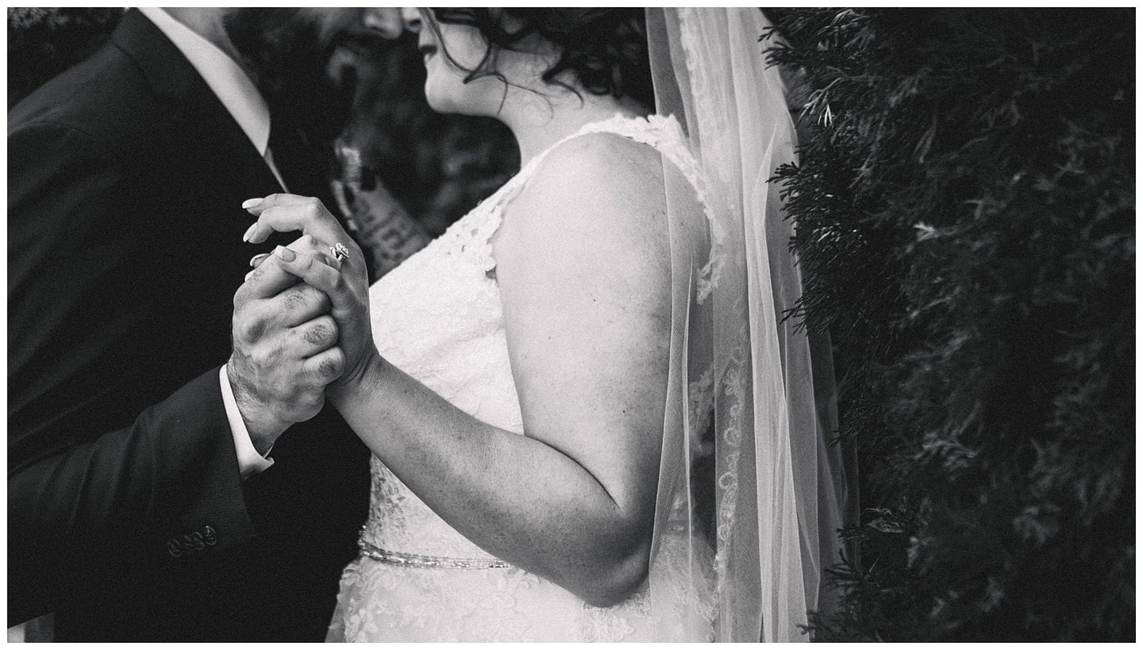 Premier Snohomish & Seattle Wedding Photographer | GSquared Weddings Photography Black-and-white photo of a bride and groom holding hands while dancing at their Snohomish wedding, with the bride in a lace dress and veil, and the groom wearing a suit. Their faces are partially visible and close together.                                   | Serving Snohomish, Seattle ,                  & Beyond