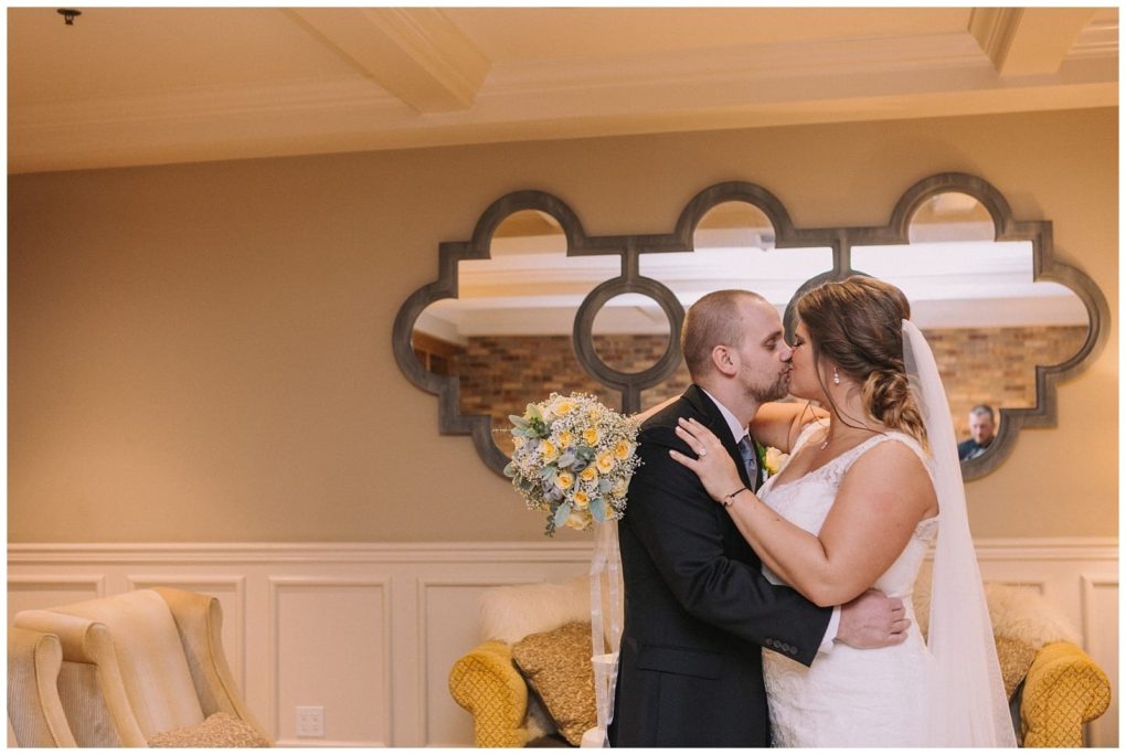 Premier snohomish & seattle wedding photographer | gsquared weddings photography a bride and groom share a kiss indoors at their snohomish seattle wedding standing in front of a decorative mirror The bride wears a white dress and veil the groom is in a black suit and a bouquet of yellow and white flowers is visible nearby | serving snohomish seattle                   & beyond