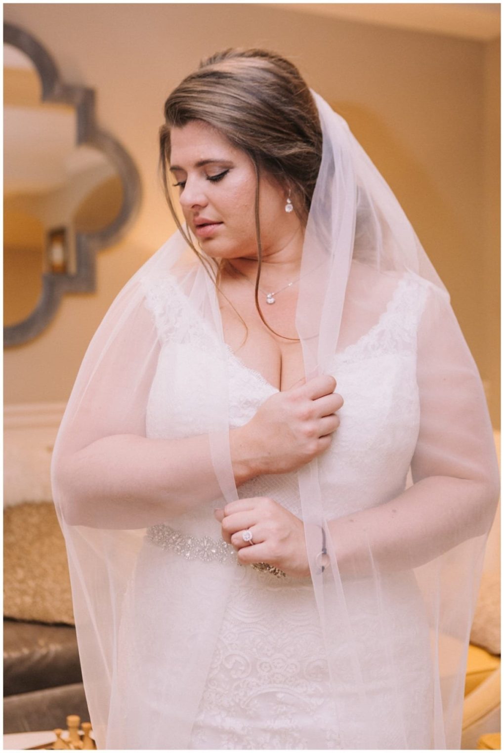Premier snohomish & seattle wedding photographer | gsquared weddings photography a bride in a white lace wedding dress and veil looks down thoughtfully holding the veil with one hand Her long brown hair is elegantly styled and she wears delicate jewelry capturing a serene moment at her snohomish seattle wedding indoors | serving snohomish seattle                   & beyond