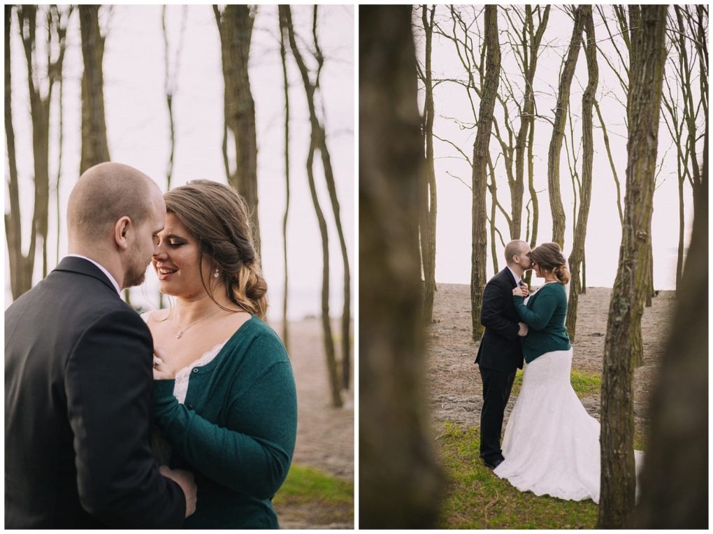 Premier snohomish & seattle wedding photographer | gsquared weddings photography a couple stands close together among bare trees the woman in a white dress and green cardigan the man in a black suit They share an intimate snohomish engagement moment outdoors with the beach and water in the background | serving snohomish seattle                   & beyond
