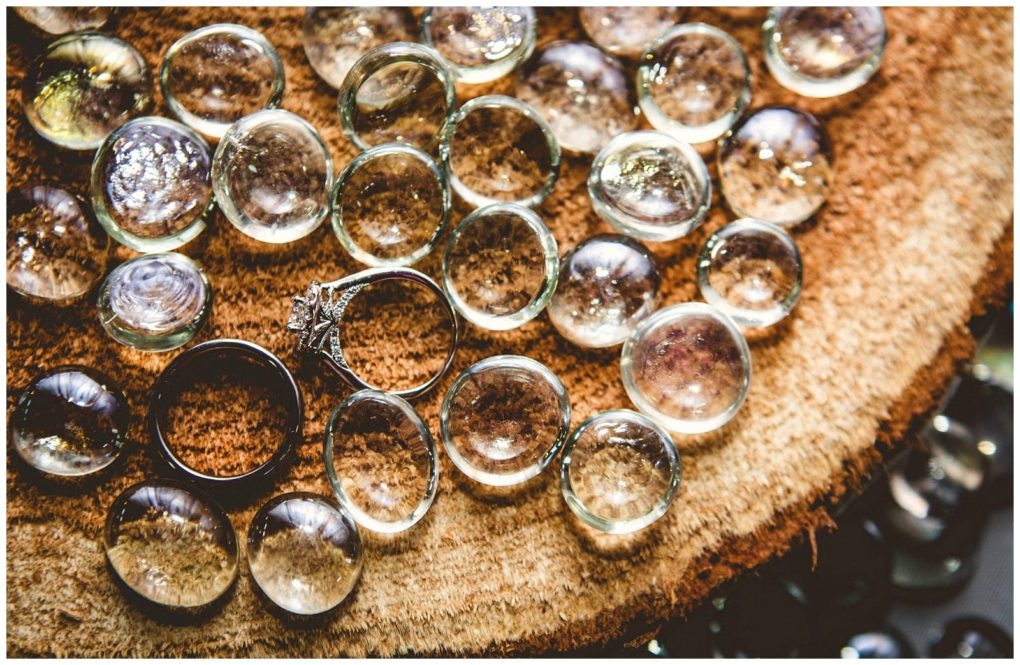 Premier snohomish & seattle wedding photographer | gsquared weddings photography clear glass marbles and two ringsone with a decorative setting one plainare arranged on a textured wooden surface Sunlight highlights the marbles creating reflections and a warm rustic atmosphere perfect for a snohomish seattle wedding engagement | serving snohomish seattle                   & beyond