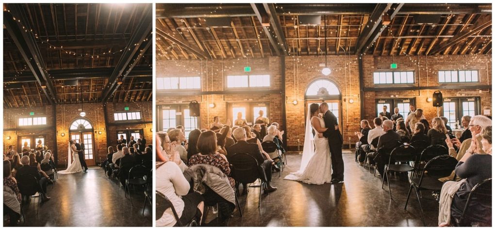 Premier snohomish & seattle wedding photographer | gsquared weddings photography a bride and groom share their first kiss at their snohomish wedding ceremony surrounded by seated guests in a rustic venue with exposed brick walls wooden beams and string lights | serving snohomish seattle                   & beyond