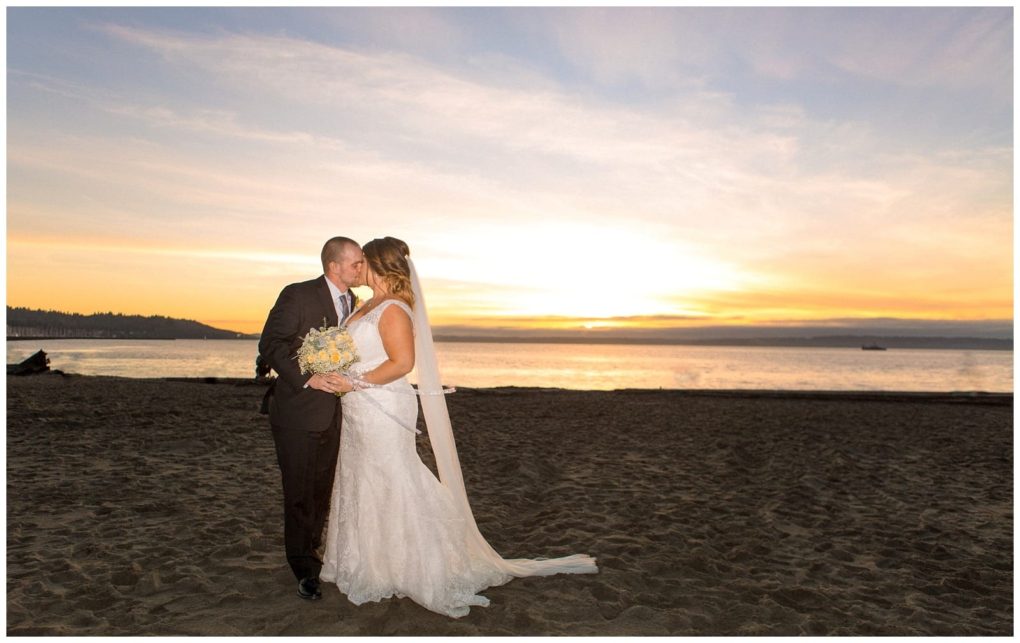 Premier snohomish & seattle wedding photographer | gsquared weddings photography a bride and groom stand on a sandy beach near seattle at sunset embracing and kissing The brides veil flows as she holds her bouquet the groom wears a dark suit Soft sky colors capture their romantic wedding engagement moment | serving snohomish seattle                   & beyond