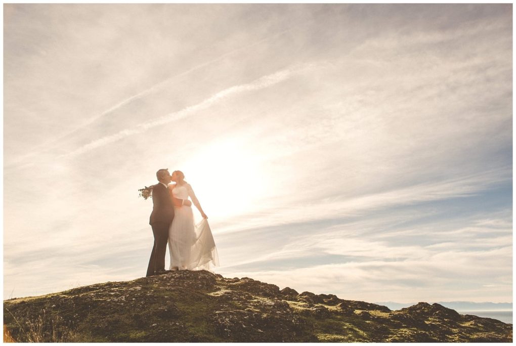 Premier snohomish & seattle wedding photographer | gsquared weddings photography a bride and groom share a kiss on a rocky hilltop under a bright sunlit sky near snohomish their veil and dress flowing in the breezecapturing a romantic seattle wedding moment against wispy clouds | serving snohomish seattle                   & beyond