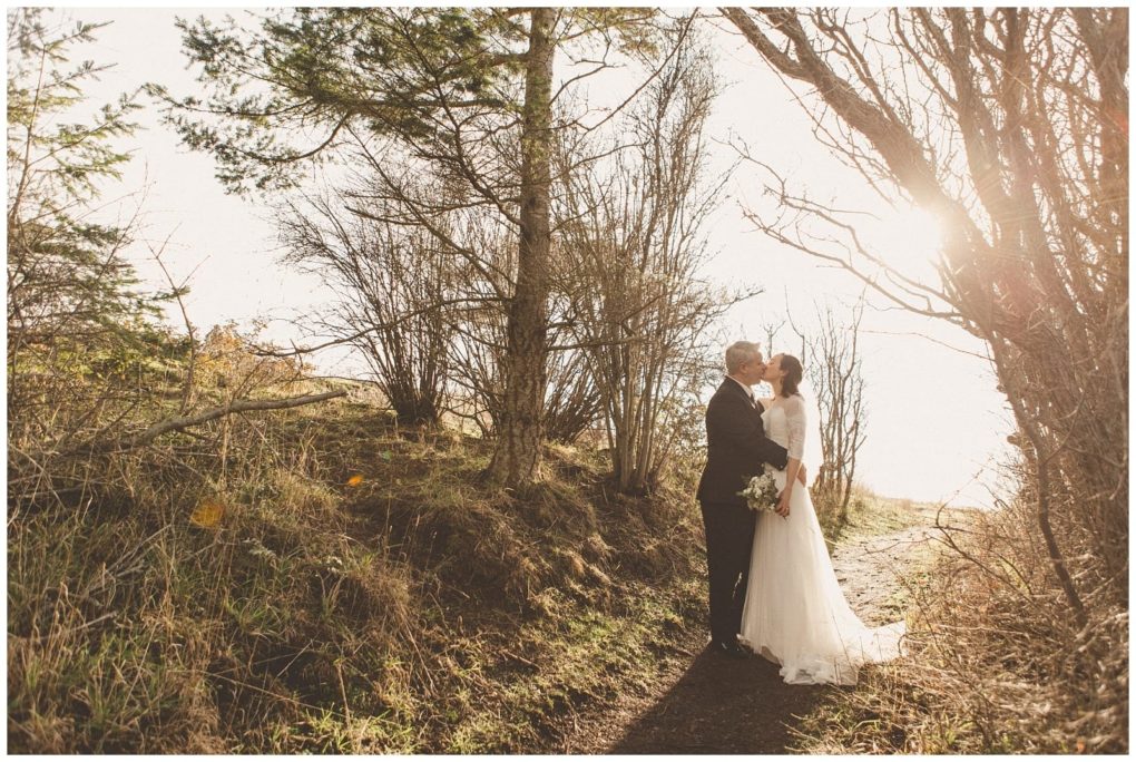 Premier snohomish & seattle wedding photographer | gsquared weddings photography a bride and groom stand together on a sunlit forest path in snohomish embracing and gazing at each other The bride holds a bouquet as sunlight streams through the bare trees capturing the magic of their seattle wedding engagement | serving snohomish seattle                   & beyond