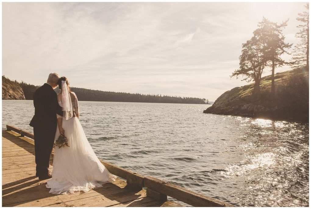 Premier snohomish & seattle wedding photographer | gsquared weddings photography a bride and groom stand on a wooden dock by the water in snohomish sharing a quiet moment The sun shines brightly casting a warm glow on their peaceful seattle wedding scene as the bride holds her bouquet | serving snohomish seattle                   & beyond