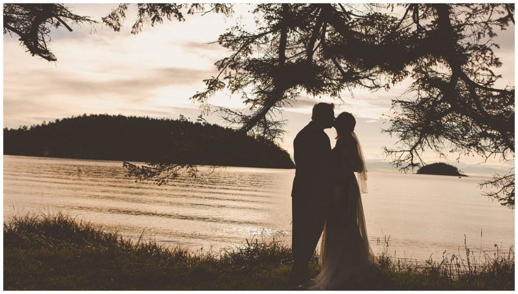 Premier snohomish & seattle wedding photographer | gsquared weddings photography silhouette of a couple embracing under tree branches by a calm lake at sunset with distant islands and a soft golden skyperfect for a snohomish seattle wedding or engagement moment | serving snohomish seattle                   & beyond