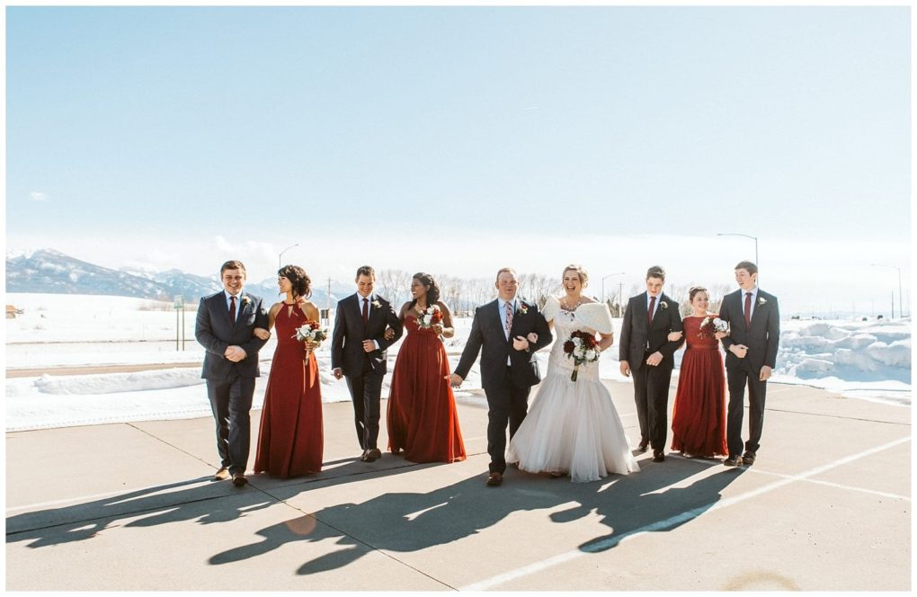 Premier snohomish & seattle wedding photographer | gsquared weddings photography a bride and groom walk outdoors with their wedding party at a scenic snohomish seattle wedding Bridesmaids in red dresses and groomsmen in dark suits pose against snowy mountains under a clear sky creating a stunning engagement photo | serving snohomish seattle                   & beyond
