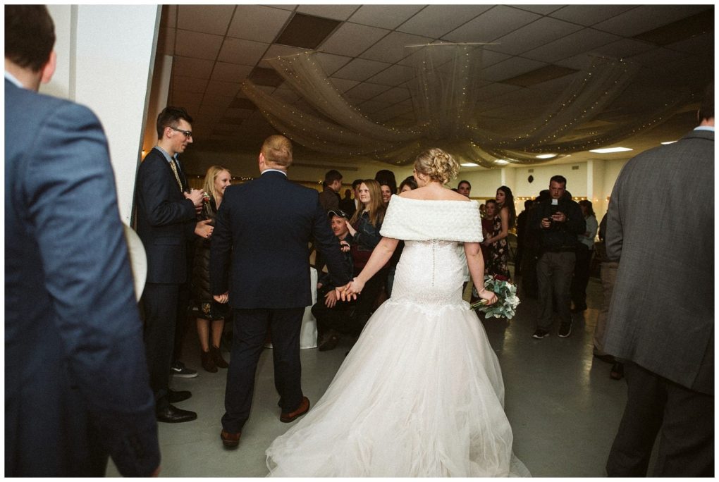 Premier snohomish & seattle wedding photographer | gsquared weddings photography a bride in a white wedding gown holds hands with her groom as they walk into a snohomish wedding reception hall filled with guests in formal attire String lights and draped fabric decorate the ceiling | serving snohomish seattle                   & beyond