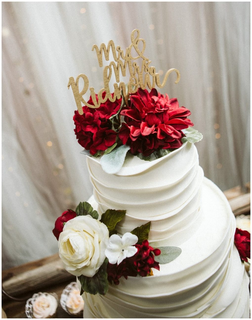 Premier snohomish & seattle wedding photographer | gsquared weddings photography a white tiered wedding cake decorated with red and white flowers topped with a gold mr & mrs ridgway sign stands before a softly lit curtain backdropperfect for a romantic snohomish or seattle wedding engagement celebration | serving snohomish seattle                   & beyond