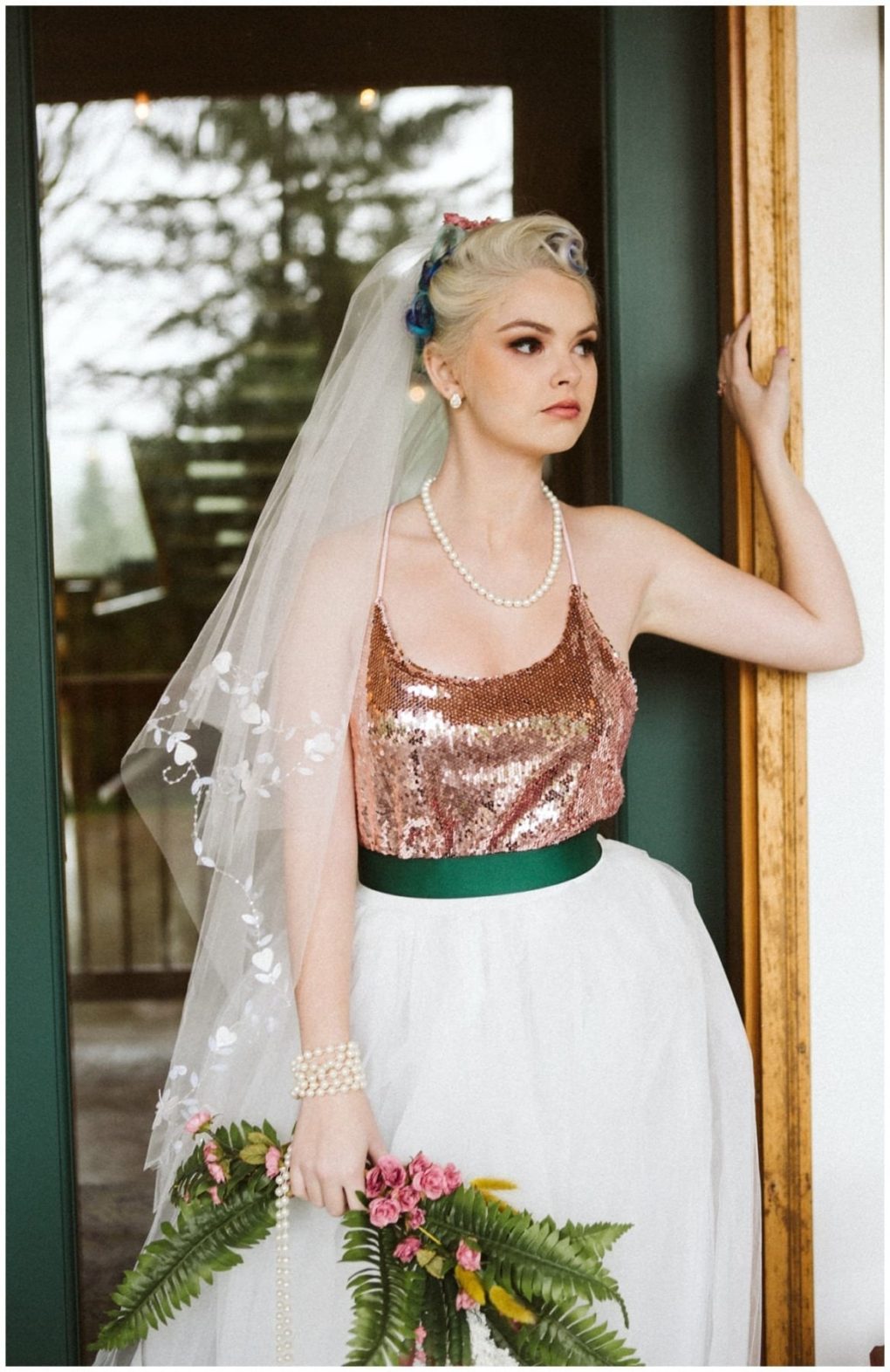 Premier snohomish & seattle wedding photographer | gsquared weddings photography a bride with light hair and a floral headpiece stands in a doorway at her snohomish seattle wedding wearing a sheer veil pearl necklace rose gold sequin top white skirt with green belt and holding a bouquet of ferns and pink flowers | serving snohomish seattle                   & beyond