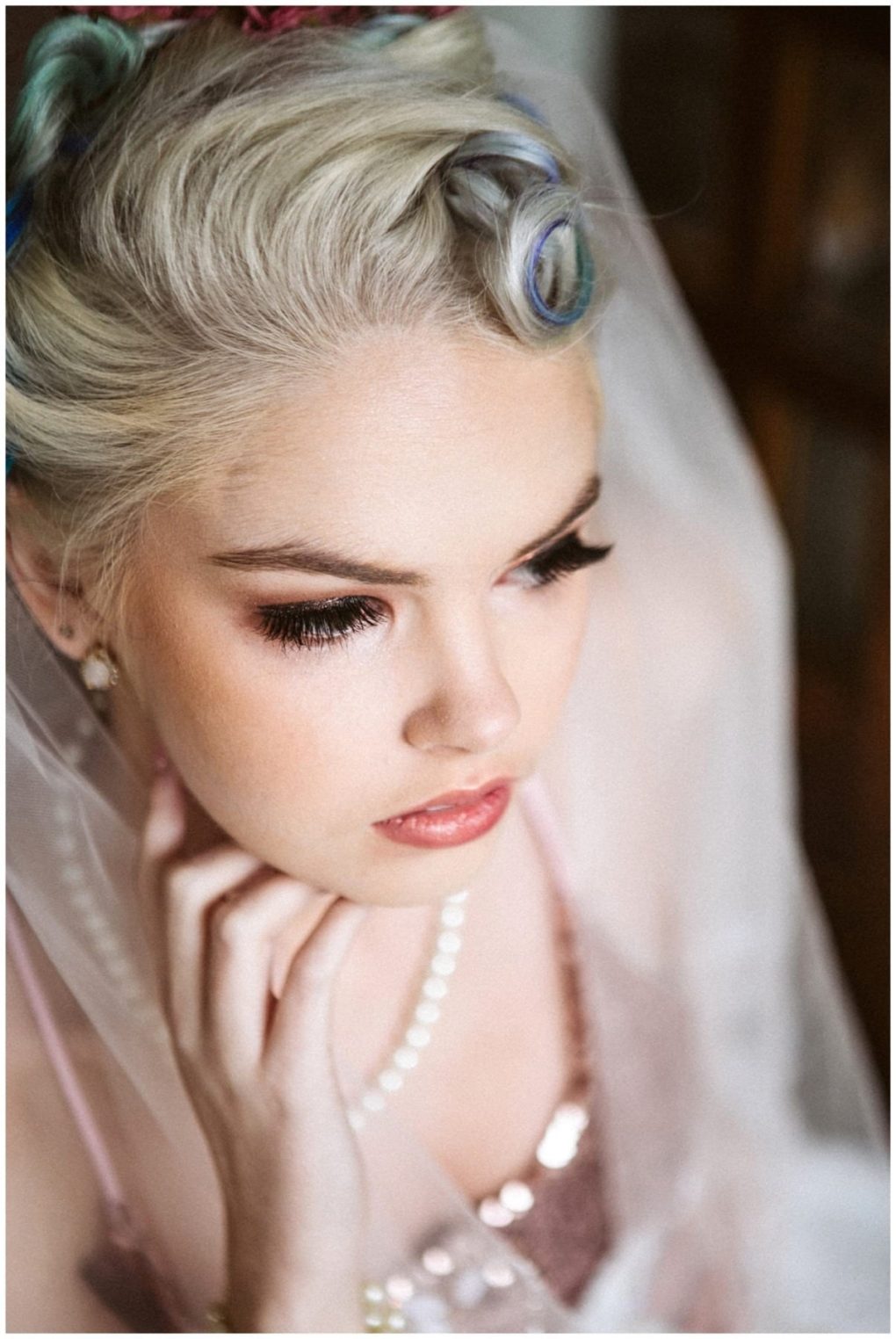 Premier snohomish & seattle wedding photographer | gsquared weddings photography a close up of a young woman with platinum blonde hair styled in vintage curls dramatic makeup and a pearl necklace captures the elegance of a snohomish seattle wedding engagement as she gazes downward her hand gently touching her chin | serving snohomish seattle                   & beyond