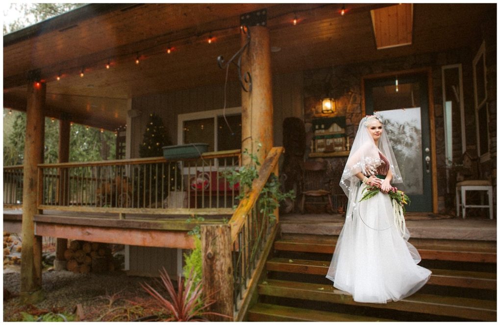 Premier snohomish & seattle wedding photographer | gsquared weddings photography a bride in a white wedding dress and veil stands holding a bouquet on wooden steps in front of a rustic porch decorated with string lights and a christmas tree perfect for a magical snohomish seattle wedding or engagement | serving snohomish seattle                   & beyond