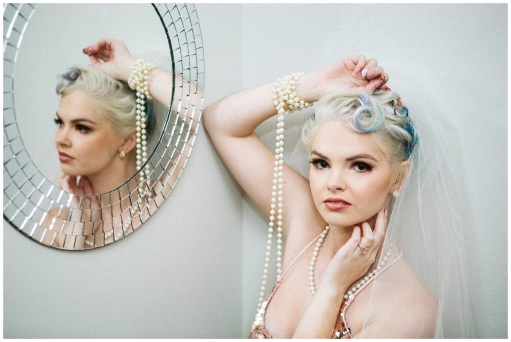 Premier snohomish & seattle wedding photographer | gsquared weddings photography a bride with vintage styled platinum blonde hair and a veil poses by a round mosaic mirror at her snohomish seattle wedding wearing layered pearl necklaces and looking thoughtfully at the camera her reflection visible in the mirror | serving snohomish seattle                   & beyond