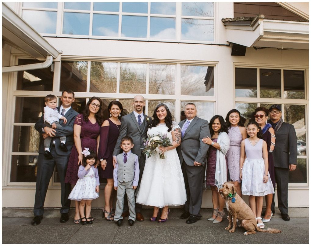 Premier snohomish & seattle wedding photographer | gsquared weddings photography a wedding party stands together outside a building at a snohomish seattle wedding The bride in a white dress and groom in a gray suit with purple accents are at the center surrounded by smiling family and a small brown dog in front | serving snohomish seattle                   & beyond