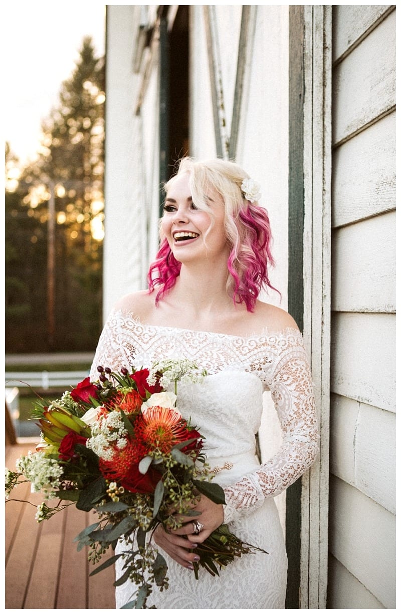 Premier snohomish & seattle wedding photographer | gsquared weddings photography a smiling bride with pink and blonde hair holds a vibrant bouquet while wearing a lace off the shoulder wedding dress standing outside a white wooden building at sunset during her enchanting snohomish seattle wedding | serving snohomish seattle                   & beyond
