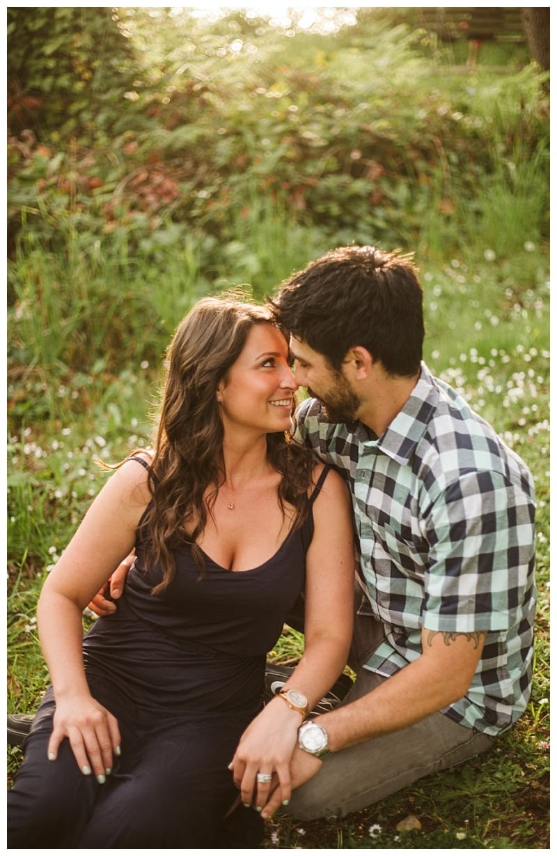 Premier snohomish & seattle wedding photographer | gsquared weddings photography a couple sits closely together outdoors on grass in snohomish smiling and gazing into each others eyes The woman wears a sleeveless navy dress the man a checked shirtsunlight and greenery create a warm seattle wedding engagement atmosphere | serving snohomish seattle                   & beyond