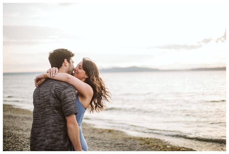 Premier snohomish & seattle wedding photographer | gsquared weddings photography a couple embraces and smiles at each other on a beach near seattle with gentle waves and a bright sky in the backgroundcapturing a perfect snohomish engagement moment | serving snohomish seattle                   & beyond