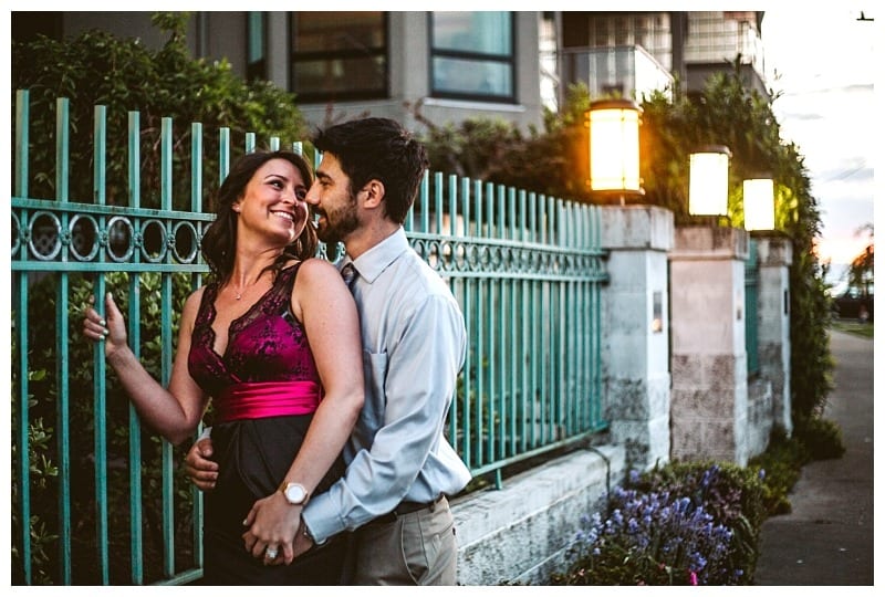 Premier snohomish & seattle wedding photographer | gsquared weddings photography a couple stands close together smiling and embracing in front of a teal metal fence and lit lanterns on a city streetcapturing a perfect snohomish seattle wedding engagement moment with greenery and buildings in the background | serving snohomish seattle                   & beyond
