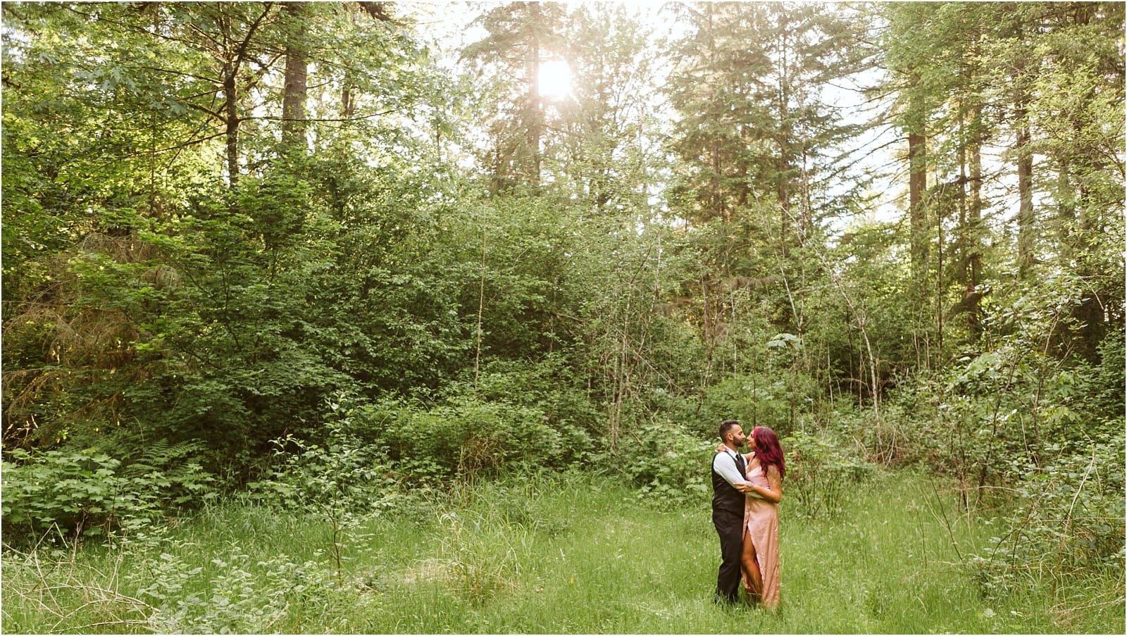 Premier Snohomish & Seattle Wedding Photographer | GSquared Weddings Photography A couple stands embracing in a sunlit forest clearing near Snohomish, surrounded by lush green trees and grass, with sunlight streaming through the branches—a perfect Seattle wedding engagement moment.                                   | Serving Snohomish, Seattle ,                  & Beyond