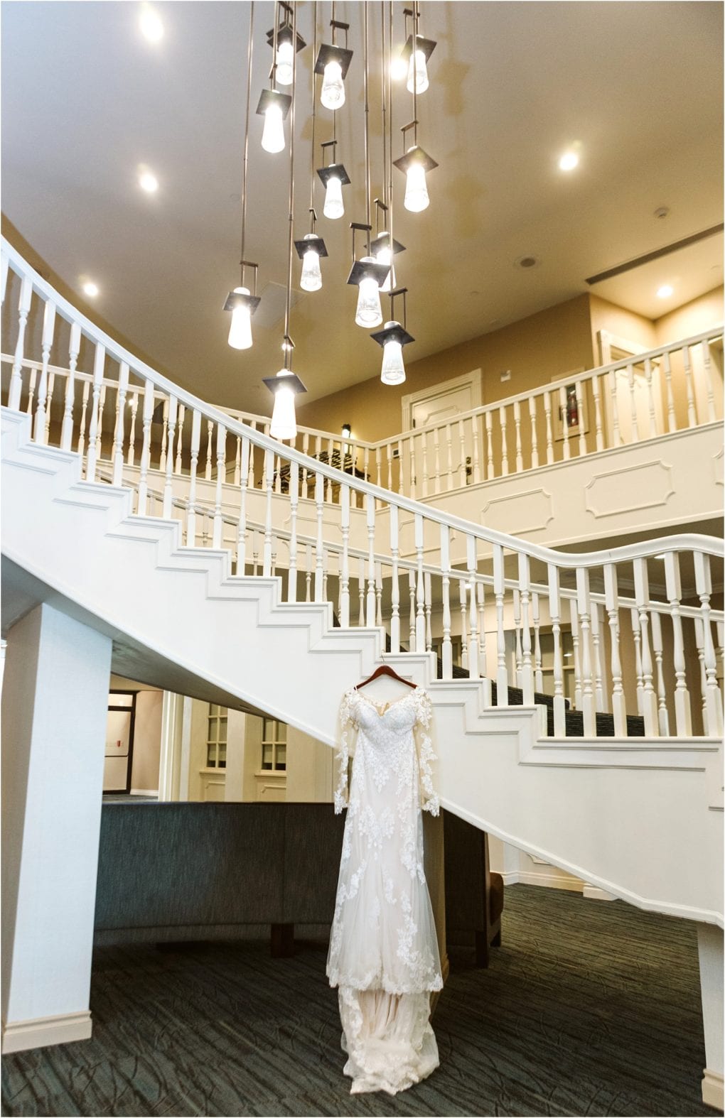 Premier snohomish & seattle wedding photographer | gsquared weddings photography a white lace wedding dress on a hanger is displayed under a white staircase with ornate railings beneath modern hanging lights in a spacious elegant interiorperfect inspiration for your snohomish seattle wedding or engagement | serving snohomish seattle                   & beyond