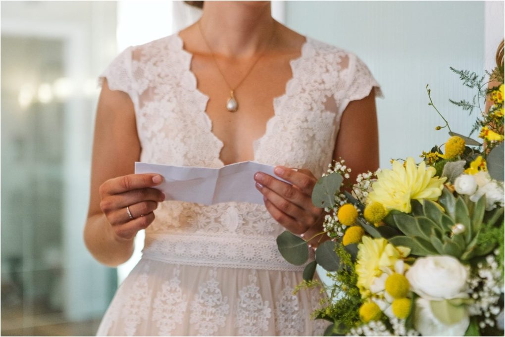 Premier snohomish & seattle wedding photographer | gsquared weddings photography a bride in a lace wedding dress holds a folded piece of paper possibly vows or a speech standing beside a bouquet of yellow and white flowers at her snohomish seattle wedding Her face is not visible | serving snohomish seattle                   & beyond