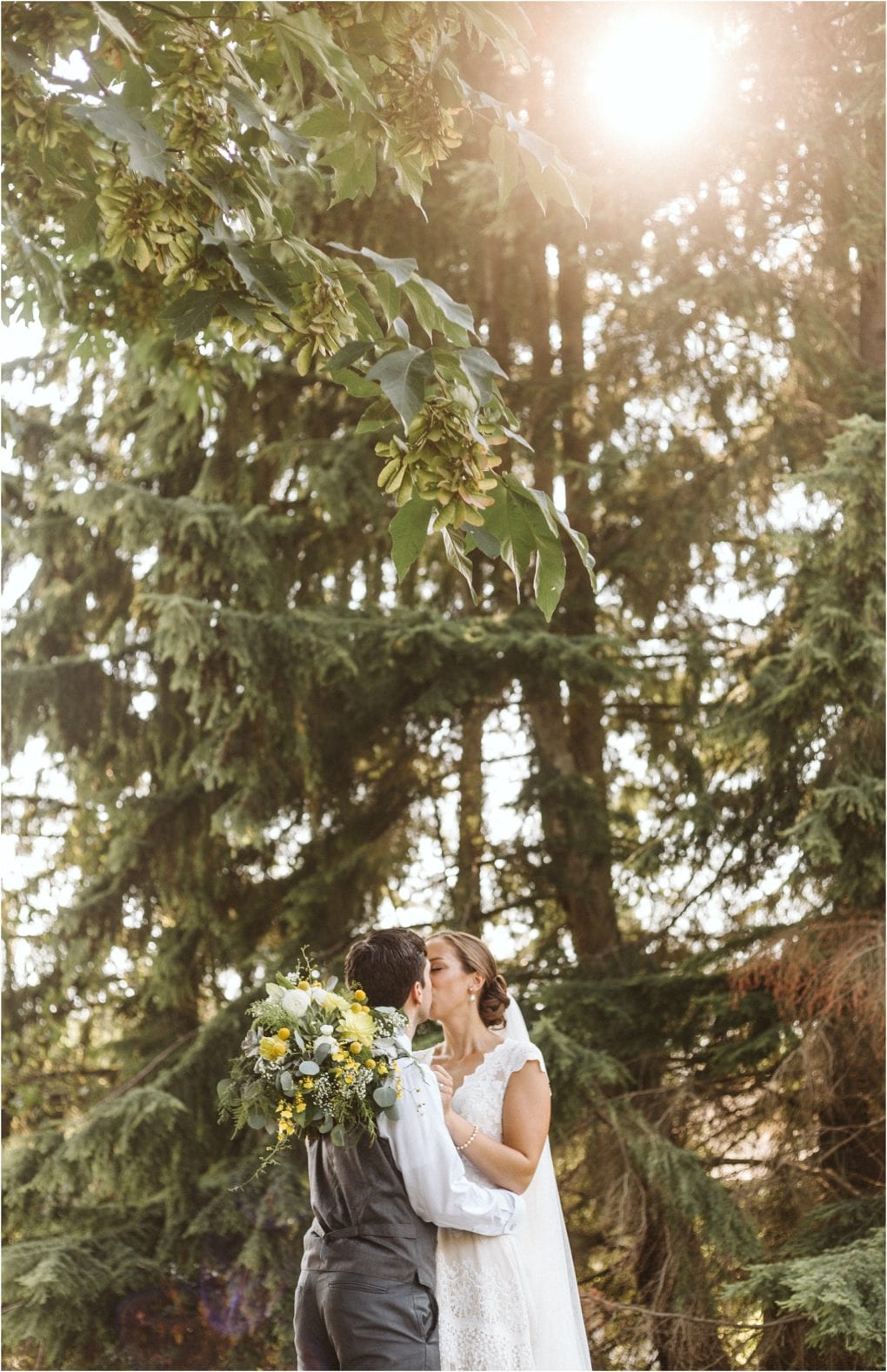 Premier snohomish & seattle wedding photographer | gsquared weddings photography a newlywed couple embraces and kisses outdoors under tall trees with sunlight streaming through the leaves Capturing a romantic snohomish seattle wedding the bride holds a bouquet in her white dress as the groom stands beside her in vest and shirt | serving snohomish seattle                   & beyond