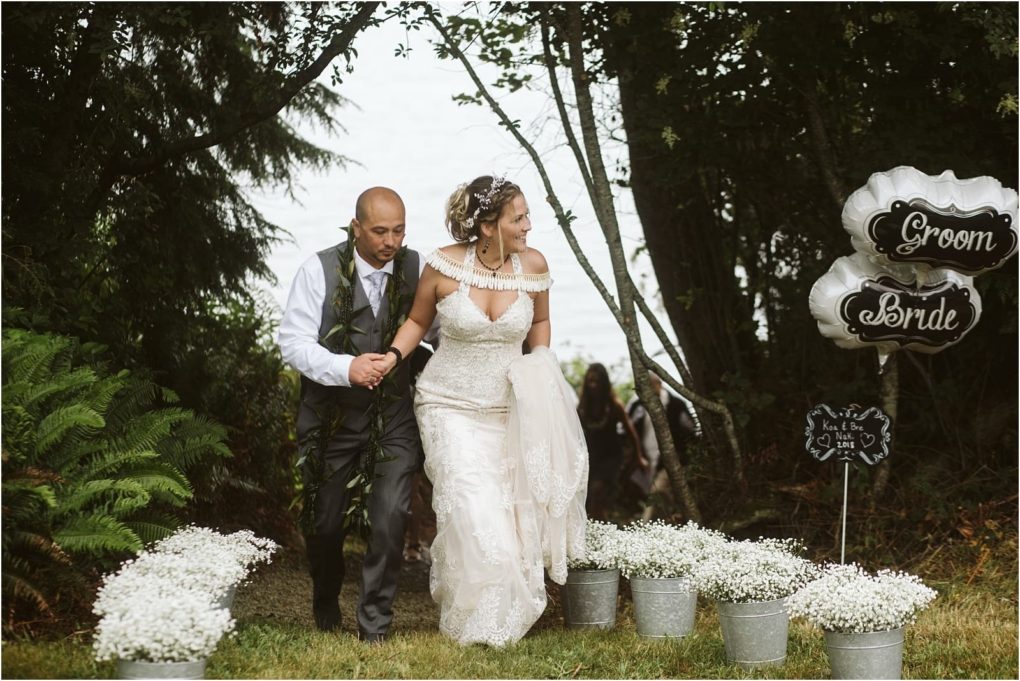 Premier snohomish & seattle wedding photographer | gsquared weddings photography a snohomish bride and groom walk up a wooded path lined with white flowers in metal buckets The bride holds her dress and the groom helps her Silver groom and bride balloons are visible beside them at this seattle wedding | serving snohomish seattle                   & beyond