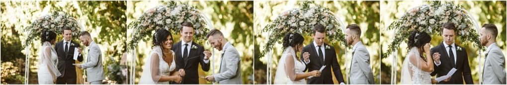 Premier snohomish & seattle wedding photographer | gsquared weddings photography a bride and groom stand under a floral arch during their outdoor snohomish wedding ceremony smiling and holding hands as the officiant reads from a paper Sunlight filters through green trees in the background | serving snohomish seattle                   & beyond