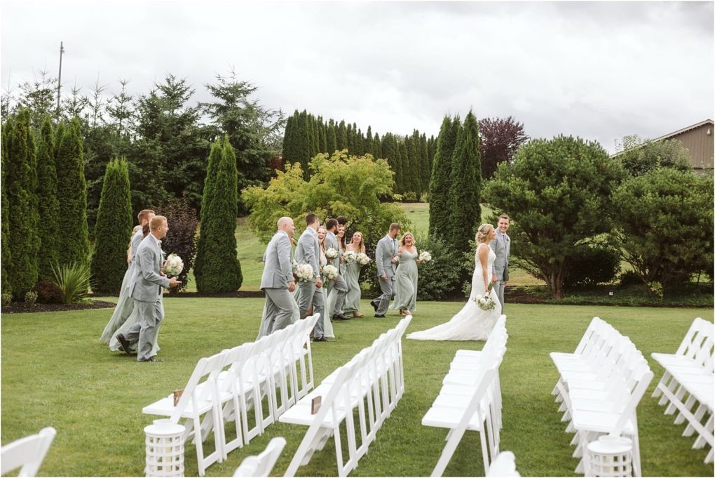 Premier snohomish & seattle wedding photographer | gsquared weddings photography a bride in a white dress and groom in a gray suit walk with their wedding party all dressed in gray across a grassy area at this scenic snohomish seattle wedding surrounded by empty white chairs and lush greenery | serving snohomish seattle                   & beyond