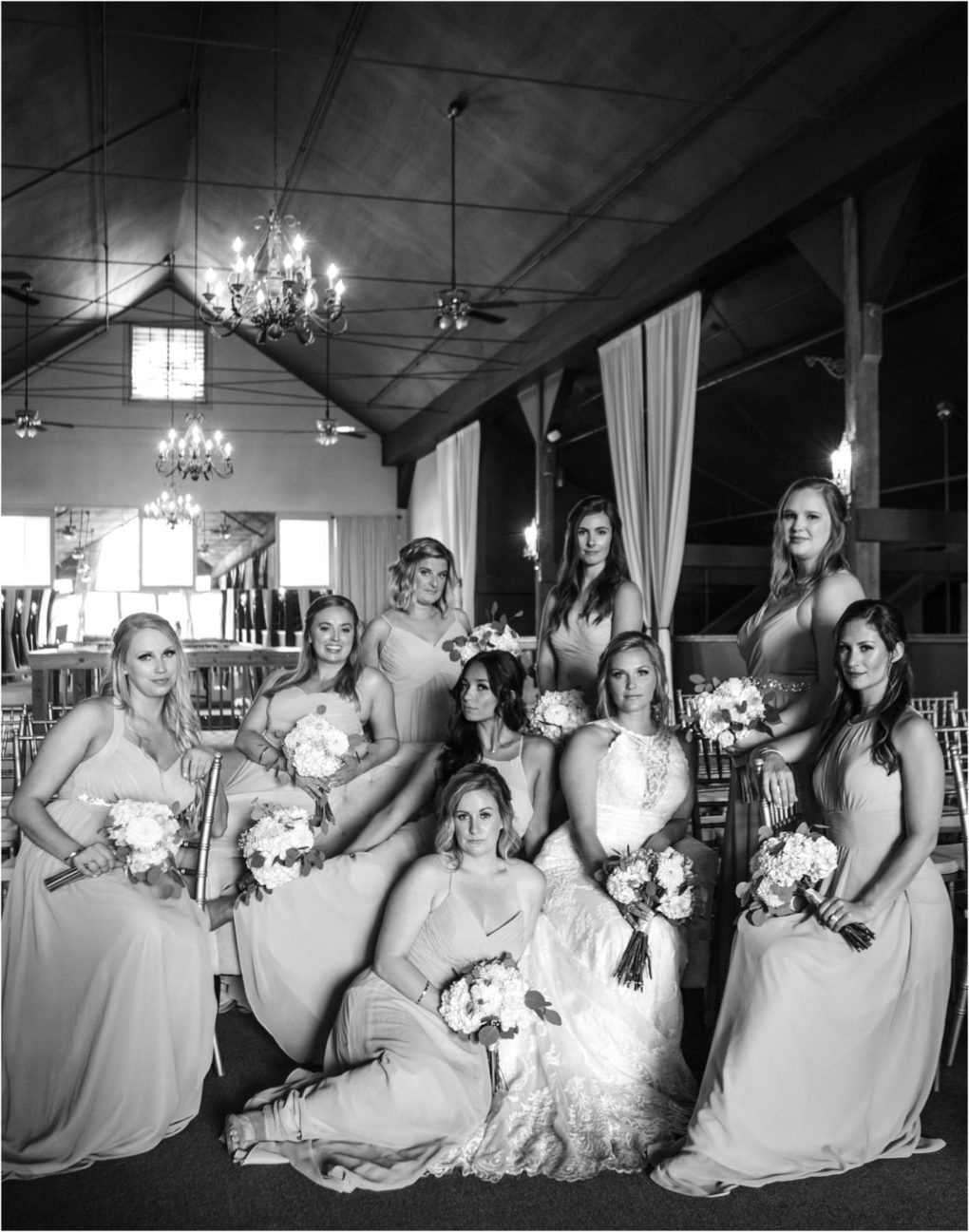 Premier snohomish & seattle wedding photographer | gsquared weddings photography a black and white photo of a bride in a lace gown seated with her bridesmaids in matching dresses all holding bouquets posing formally at an elegant chandelier lit indoor snohomish or seattle wedding venue | serving snohomish seattle                   & beyond