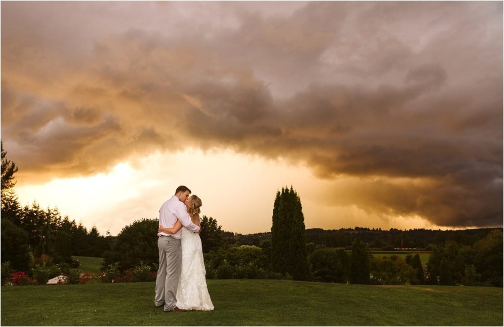 Premier snohomish & seattle wedding photographer | gsquared weddings photography a bride and groom embrace on a grassy lawn at sunset surrounded by trees and rolling hills near snohomish Dramatic cloudy skies and a glowing horizon set a romantic scene for their seattle wedding engagement | serving snohomish seattle                   & beyond