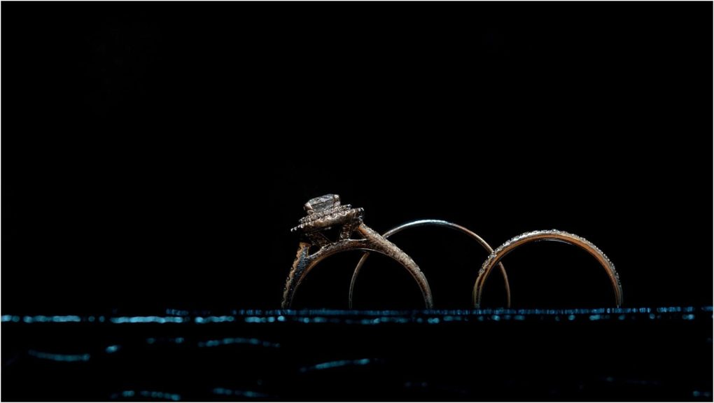 Premier snohomish & seattle wedding photographer | gsquared weddings photography three gold rings including a diamond engagement ring are displayed in a row against a black background with a subtle blue reflective surface beneath themperfect for a snohomish seattle wedding engagement | serving snohomish seattle                   & beyond