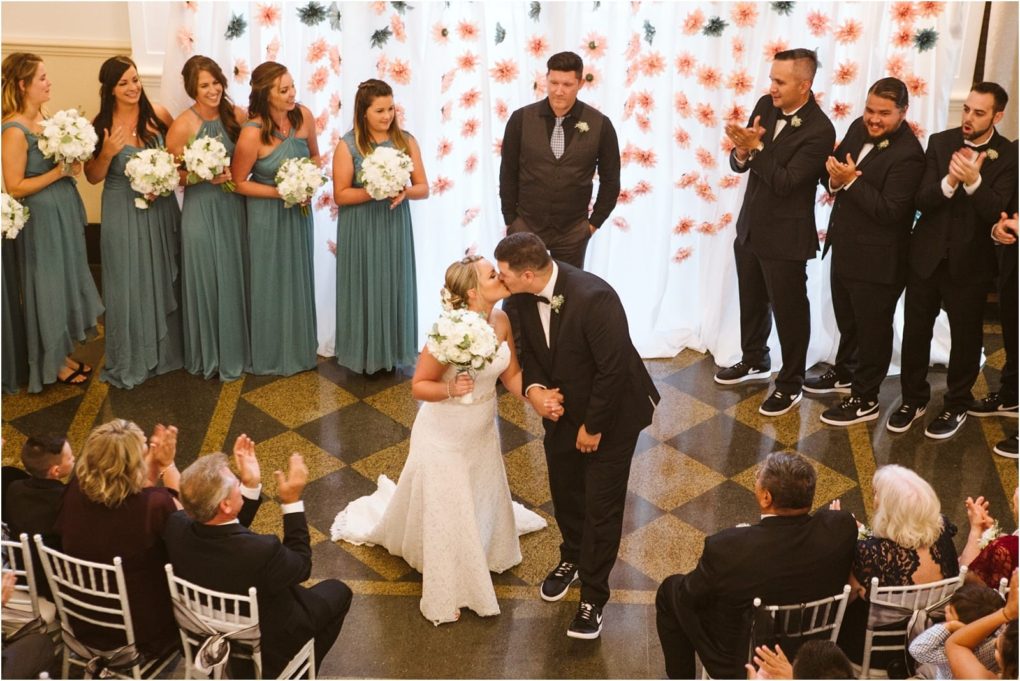 Premier snohomish & seattle wedding photographer | gsquared weddings photography a bride and groom kiss at the altar during a romantic snohomish wedding as guests clap Bridesmaids in teal dresses and groomsmen in dark suits stand on either side framed by elegant floral decorations | serving snohomish seattle                   & beyond