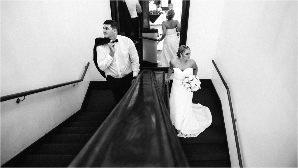 Premier snohomish & seattle wedding photographer | gsquared weddings photography a bride in a strapless white dress holds a bouquet on a staircase while her groom ready for their snohomish seattle wedding drapes his jacket over his shoulder a mirror reflects their backs Black and white photo | serving snohomish seattle                   & beyond