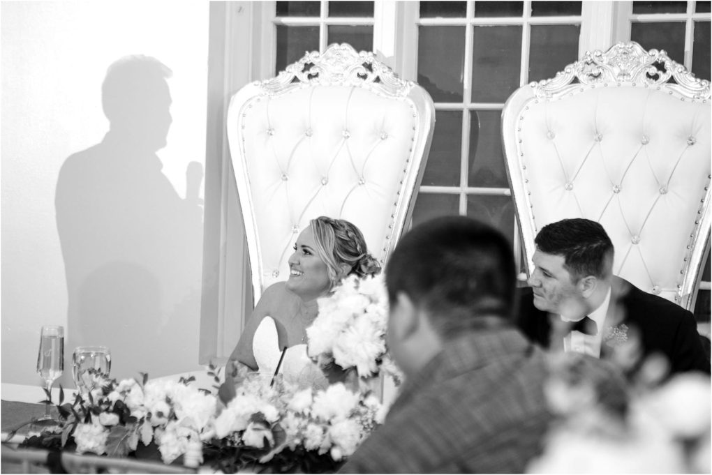 Premier snohomish & seattle wedding photographer | gsquared weddings photography a black and white photo of a bride and groom seated at an ornate table smiling as they look toward a speaker Captured at a snohomish seattle wedding the table is beautifully decorated with flowers | serving snohomish seattle                   & beyond