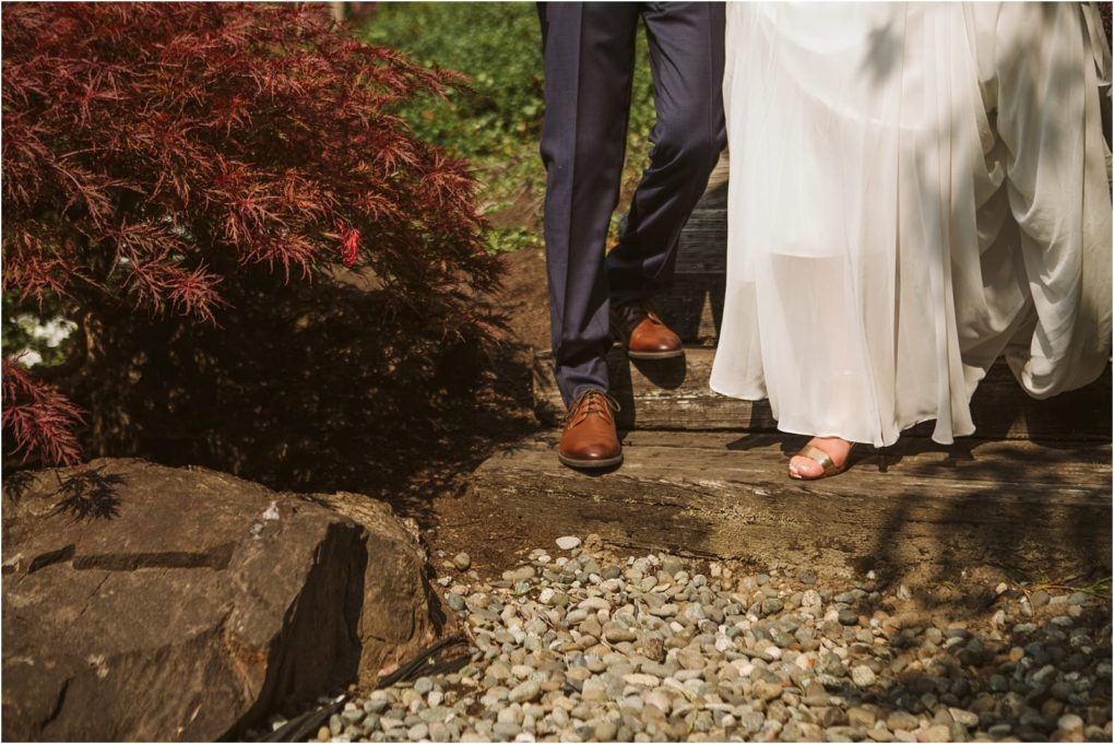 Premier snohomish & seattle wedding photographer | gsquared weddings photography a couple dressed in wedding attire walks down wooden steps outdoors at a snohomish seattle wedding only their lower bodies are visible The groom wears navy pants and brown shoes while the bride wears a white dress and open toed shoes Rocks and red foliage surround them | serving snohomish seattle                   & beyond