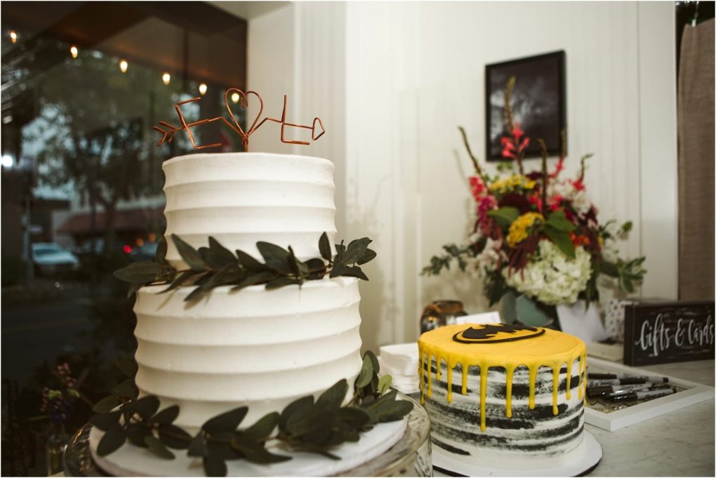 Premier snohomish & seattle wedding photographer | gsquared weddings photography two cakes on a table a white tiered cake decorated with green leaves and a heart topper perfect for a snohomish seattle wedding Next to it a smaller cake with yellow drip and batman logo Flowers and a window complete the engagement celebration scene | serving snohomish seattle                   & beyond