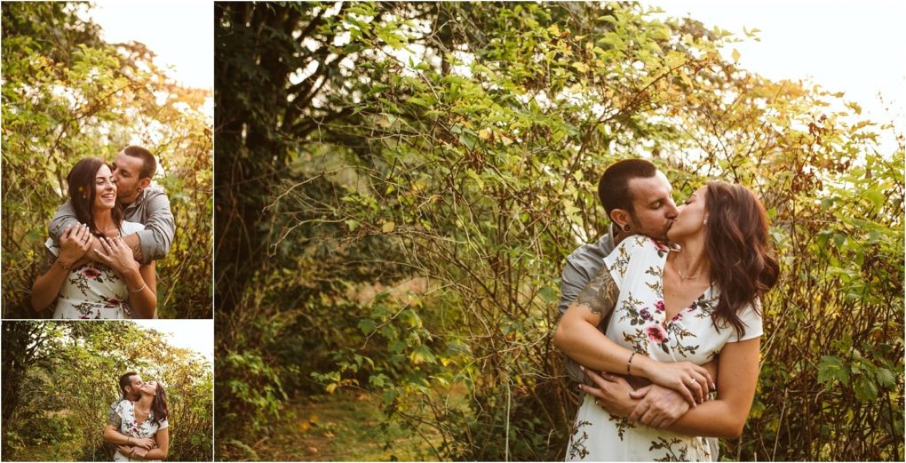 Premier snohomish & seattle wedding photographer | gsquared weddings photography a couple embraces and kisses outdoors in a sunlit leafy area during their snohomish engagement The woman wears a white floral dress the man a gray shirtthey look happy together surrounded by lush green foliage | serving snohomish seattle                   & beyond