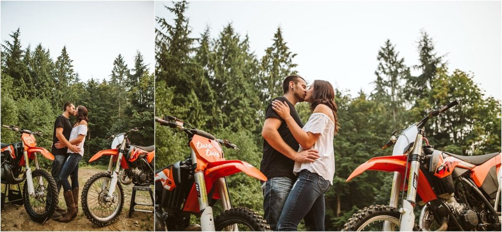 Premier snohomish & seattle wedding photographer | gsquared weddings photography a couple stands close and kisses near two orange dirt bikes surrounded by tall green trees and a forested background capturing a perfect snohomish seattle wedding engagement moment with the sky visible above | serving snohomish seattle                   & beyond