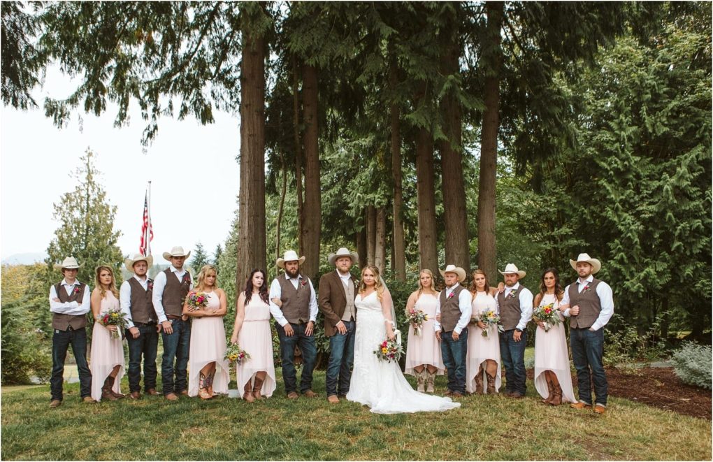 Premier snohomish & seattle wedding photographer | gsquared weddings photography a wedding party poses outdoors in front of tall trees at a snohomish celebration The bride in white stands with the groom in a vest and cowboy hat surrounded by bridesmaids in pink and groomsmen in vests and cowboy hats | serving snohomish seattle                   & beyond