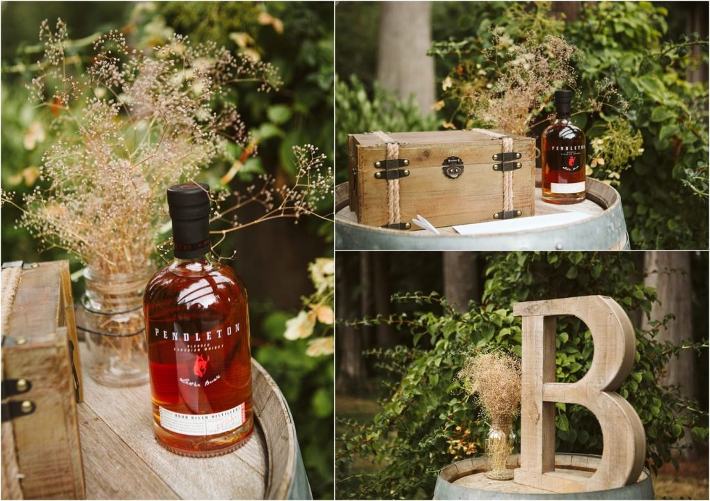 Premier snohomish & seattle wedding photographer | gsquared weddings photography a bottle of pendleton whiskey sits on a barrel beside a wooden box dried flowers in a jar and a large wooden letter b surrounded by lush greeneryperfect for a snohomish or seattle wedding or engagement outdoor setting | serving snohomish seattle                   & beyond