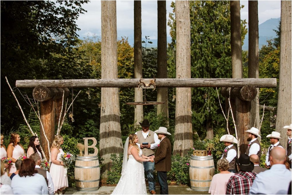 Premier snohomish & seattle wedding photographer | gsquared weddings photography a bride and groom exchange vows outdoors in a rustic woodland snohomish setting surrounded by bridesmaids in pink dresses and groomsmen in cowboy hats Large wooden beams and barrels decorate the altar area of this seattle wedding | serving snohomish seattle                   & beyond
