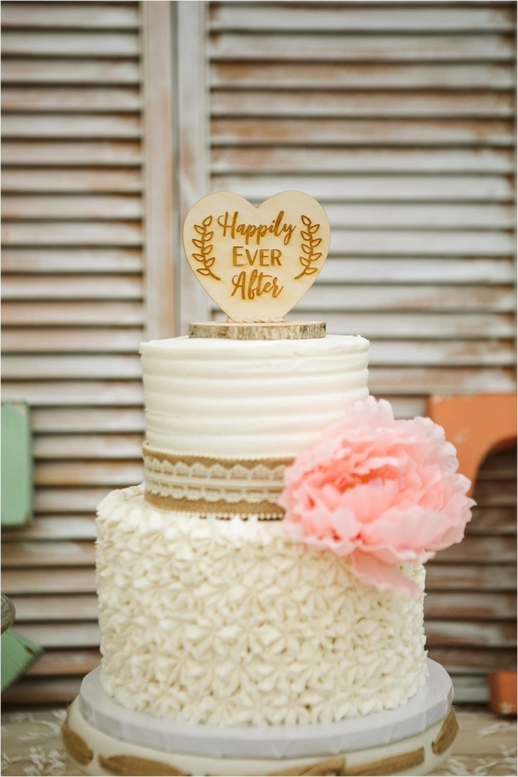 Premier snohomish & seattle wedding photographer | gsquared weddings photography a two tier white cake decorated with textured icing a large pink flower burlap ribbon and a wooden topper that reads happily ever afterperfect for a snohomish seattle wedding or engagementdisplayed in front of wooden shutters | serving snohomish seattle                   & beyond