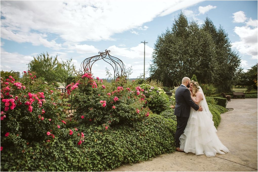 Premier snohomish & seattle wedding photographer | gsquared weddings photography a bride and groom stand together in an outdoor garden near snohomish surrounded by blooming pink roses and greenery under a partly cloudy blue skya perfect seattle wedding engagement moment | serving snohomish seattle                   & beyond