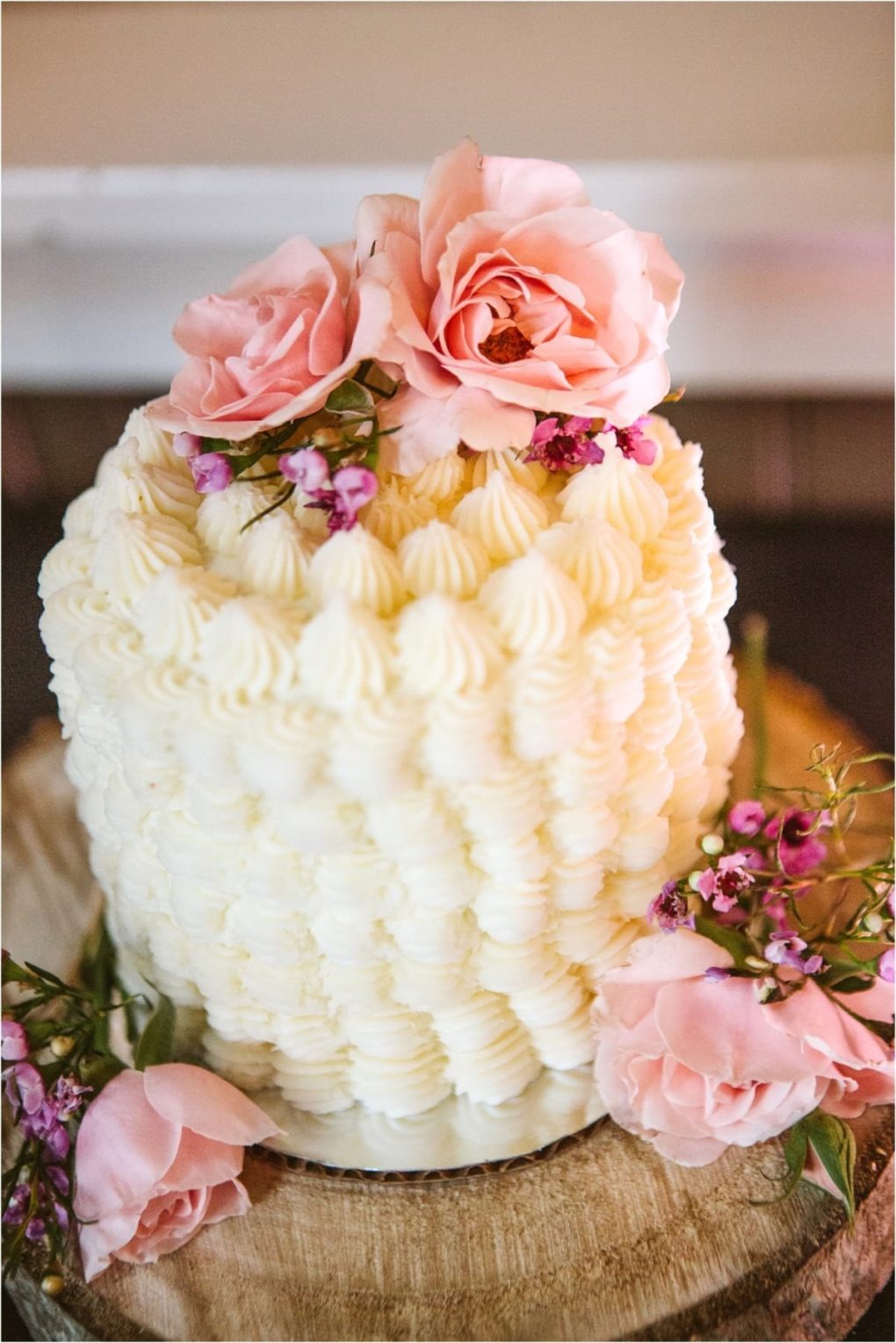 Premier snohomish & seattle wedding photographer | gsquared weddings photography a tall white cake decorated with textured piped frosting topped and surrounded by pink roses and small purple flowers sits on a wooden standperfect for a romantic snohomish or seattle wedding engagement | serving snohomish seattle                   & beyond